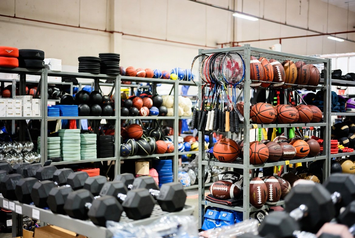 Assorted sporting goods on display — dumbbells, footballs, and rackets arranged on shelves